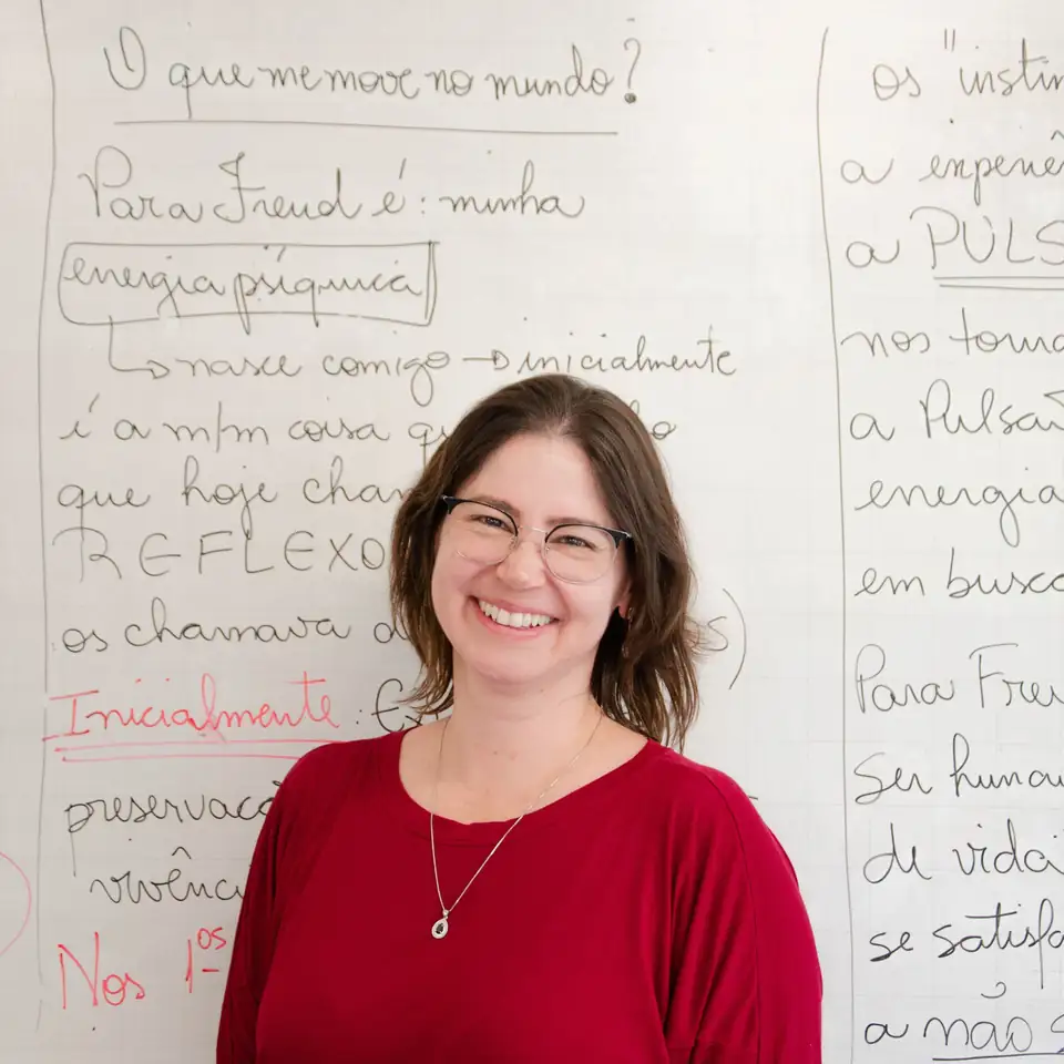 Professora sorrindo diante de um quadro em sala de aula